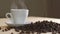 Close up of white cup of evaporating coffee on table near roasted beans. Slowly