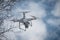 Close up of white drone flying in the air with tree and cloudy sky in the background. Hobby quadrocopter with camera