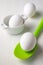 Close-up of white eggs and green silicone spoon, with selective focus, on white wooden table