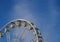 Close up of a white ferris wheel with enclosed gondola cars against a bright blue sky