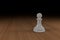 Close up of a white, glass, chess pawn on a wooden surface
