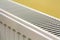 Close-up of white heating radiator detail on light yellow wall copy space background. Comfortable warm home interior, climate