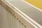 Close-up of white heating radiator detail on light yellow wall copy space background. Comfortable warm home interior, climate