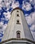 Close up of a white lighthouse with 4 windows on top of each other. Background with blue sky and white clouds. Portrait