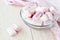 Close-up of white pink fluffy marshmallows in a glass bowl on a light wooden table. Sweet and tasty winter food. Delicious soft