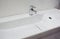 A close-up of a white porcelain ceramic shallow rectangle wall mounted bathroom sink, basin with a right side chrome water faucet