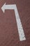 Close-up of white road marking arrow pointing to left on maroon paving flag