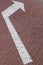 Close-up of white road marking arrow pointing to right on maroon paving flag