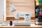 Close-up of a white sewing machine with a purple thread and crates with yarn by a window in a bright crafts room interior. Real ph