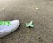 Close up white sneaker next to a fallen leaf on the street during autumn.