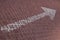 Close-up of white straight road marking arrow on maroon paving flag