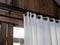 Close-up of white wall curtain on wooden curtain rail bar decorated on the wood plank wall of tropical gable building.