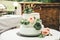 Close up of white wedding cake laying on table. Love inscription, pink rose and green leaves floral decoration. Outside