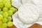 Close-up of whole head of camembert in just open paper package and sweet green grapes on a brown wooden cutting board