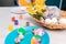 Close up of wicker basket with daffodils and plates of painting eggs on the table. Preparation for the celebration of