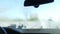Close-up windshield with water spraying on sunny day outdoors. Shooting from inside automobile cleaning vehicle with