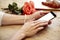 Close-up of woman beautiful hands holding mobile phone. Blank phone screen for layout. Red roses flowers behind on wooden table. S