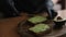Close-up of Woman in black glowes puts guacamole or avocado spread on top of rye bread toast on wooden board at home