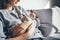 Close up of a woman in casual clothes sitting on the sofa at home and holding cute sleepy Devon Rex kitten. Cat is feeling relaxed