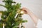 Close up of woman decorating christmas tree with goldenChristmas baubles. Copy space over white wall with lights