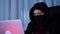 Close up of woman face in black mask and hood breaking password on computer. Hacker face looking at laptop screen and coding web s