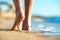 Close up of woman feet walking barefoot on sand leaving footprints on golden beach. Vacation, travel and freedom concept. People