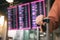 Close up of woman hand holding suitcase standing at the airport checking arrival departure board with the flight schedule in