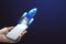 Close up of woman hand holding tablet with glowing flying blue rocket on blue background with mock up place. Start up and launch