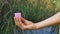 Close up of woman hand with pink silicone menstrual cup standing against green natural background with lake. Zero waste