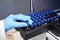 Close up woman hand in a rubber gloves put sample in a glass vial with blue cap into the autosampler rack in HPLC system