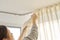 Close up of woman hands hanging curtain with metal hooks on ceiling ledge