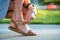 Close up of woman hands tying her open summer sandals shoes on sidewalk in sunny weather