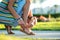 Close up of woman hands tying her open summer sandals shoes on sidewalk in sunny weather