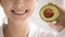 Close up woman with healthy toothy smile holding avocado