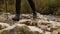 Close-up of a woman hiker`s feet crossing a stream on rocks. Green grass is visible in the background. The concept of hiking