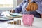 Close-up of a woman holding a coin in a pig piggy bank and recording income, expenses, ideas for calculating expenses.