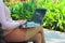 Close-up of a woman holding a laptop on her lap in the park on a bench against a background of red flowers. Freelance, student the