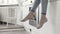 Close up for woman legs dangling with white kitchen drawers and oven on the background. Action. Women wearing jeans