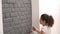 Close-up of a woman painting a brick wall in gray using a paint brush.