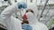 Close-up of woman in respirator adding fertiliser to plant pot. Caucasian biologist in protective uniform dripping