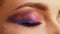 Close-up of a woman`s eye with bright shiny makeup.  The blinking eye of a girl in profile. Pink-purple sequined fashion makeup.