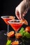 Close-up of woman`s hand with bracelets, placing orange slice in a glass of blood orange cocktail, with another in the background