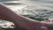 Close up of a woman\'s hand is gently touching surface waves of the sea in sunset