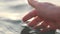 Close up of a woman\'s hand is gently touching surface waves of the sea in sunset