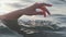 Close up of a woman\'s hand is gently touching surface waves of the sea in sunset