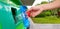 Close up woman`s hand holding and dumping plastic bottle of water into green recycle bin, trashcan or trash