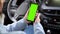 Close-up of woman\\\'s hand holding smartphone with blank screen, car steering wheel background. Mockup