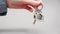 Close-up of a woman's hand in shirt shakes new keys with a metal keychain house. Gray background. The concept of
