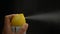 Close up of woman` s hand is spraying air freshener on black background. Yellow spray can in woman hand on dark background.