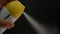 Close up of woman\'s hand is spraying air freshener on black background. Yellow spray can in woman hand on dark background.